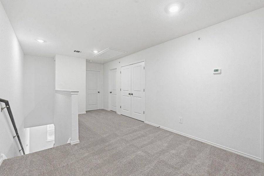 Carpeted loft area featuring white walls, recessed lighting, white doors with dark hardware, and a white thermostat Carpeted loft area featuring white walls, recessed lighting, white doors with dark hardware, and a white thermostat