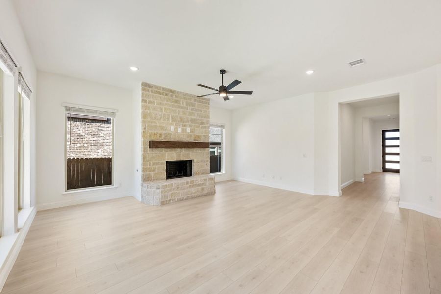 Open living room with stone fireplace, wood mantel, ceiling fan, and light hardwood floors Open living room with stone fireplace, wood mantel, ceiling fan, and light hardwood floors