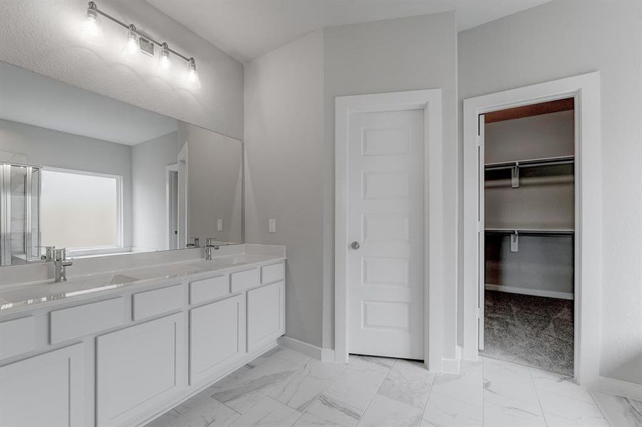 Light colored cabinets with light granite countertops complement the space, alongside a spacious walk-in closet with shelving, high ceilings, custom paint, and sleek, dark modern finishes. An ideal retreat for unwinding after a long day. Sample photo of completed home with similar floor plan. As-built interior colors and selections may vary.