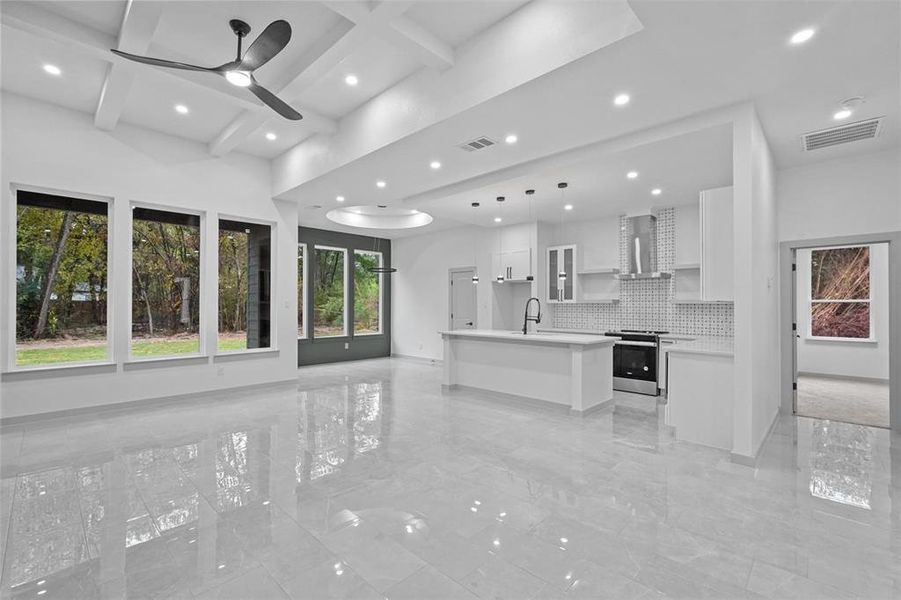 Kitchen with a kitchen island with sink, white cabinets, hanging light fixtures, stainless steel stove, and wall chimney exhaust hood