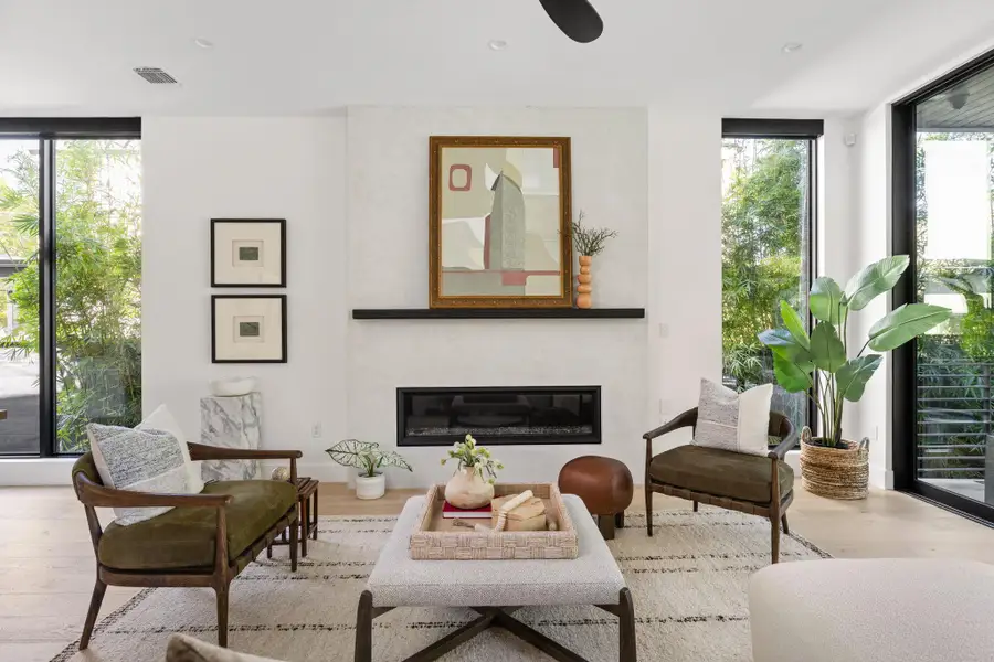 Living room featuring wood finished floors, a glass covered fireplace, floor to ceiling windows, and a ceiling fan Living room featuring wood finished floors, a glass covered fireplace, floor to ceiling windows, and a ceiling fan