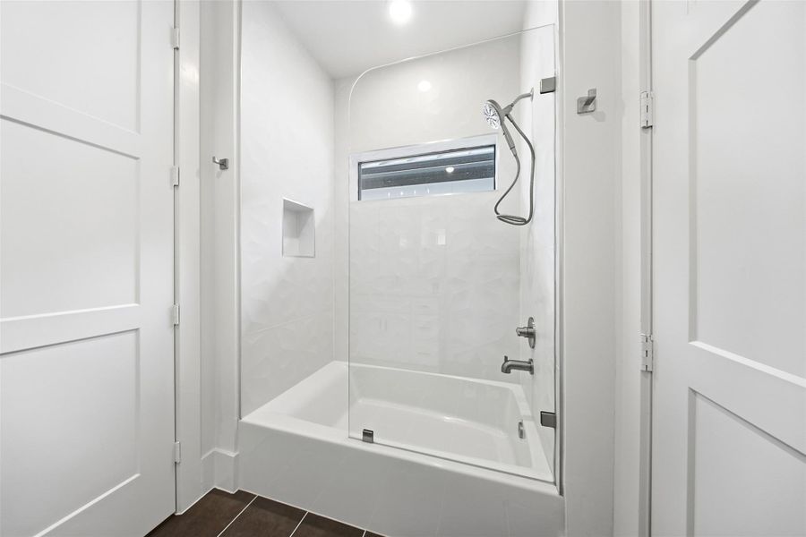 This bathroom features a deep soaking tub with a glass splash guard and a built-in wall niche for storage.