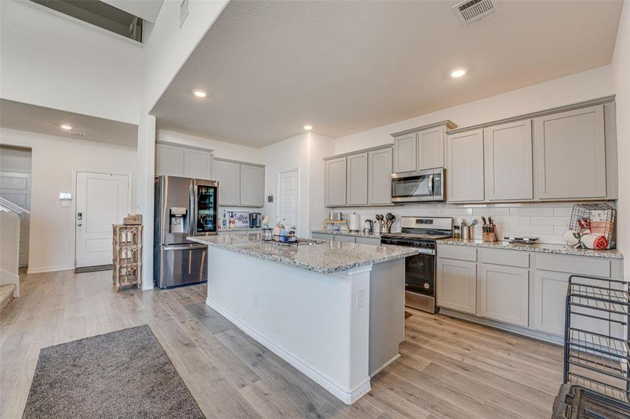 Kitchen featuring stainless steel appliances, tasteful backsplash, a center island, gray cabinetry, and light stone counters