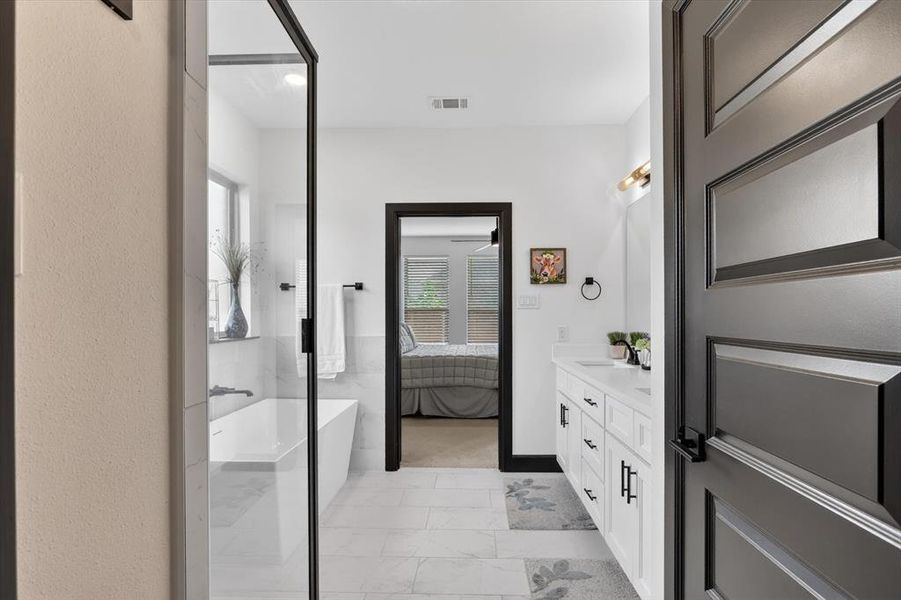 Bathroom featuring a frameless glass shower enclosure, a freestanding soaking tub, a dual vanity with undermount sinks, and white tile flooring