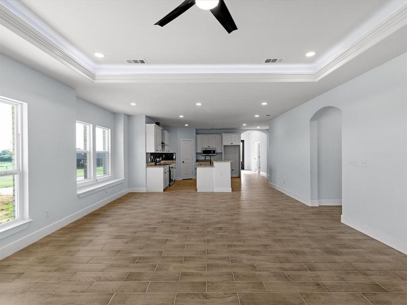 Unfurnished living room with arched walkways, recessed lighting, a ceiling fan, light wood finished floors, and a raised ceiling