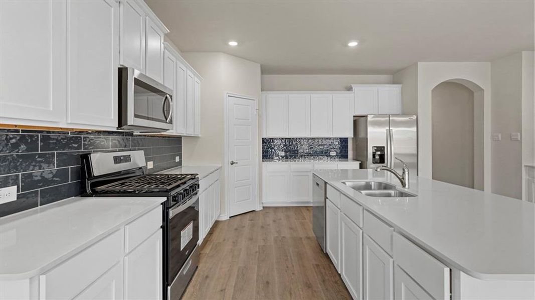 Expansive kitchen featuring white cabinetry, light countertops, wood-finish flooring, stainless steel appliances, and a dark subway tile backsplash