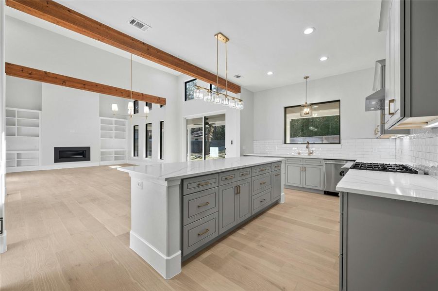 Kitchen featuring stainless steel dishwasher, pendant lighting, light stone counters, a kitchen island, and decorative backsplash