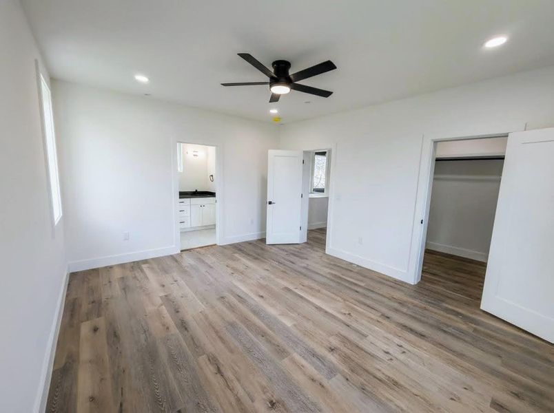 Unfurnished bedroom with a spacious closet, light wood-style floors, ceiling fan, recessed lighting, and ensuite bath