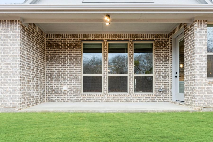 Covered back patio with brick exterior, large windows, and green lawn Covered back patio with brick exterior, large windows, and green lawn