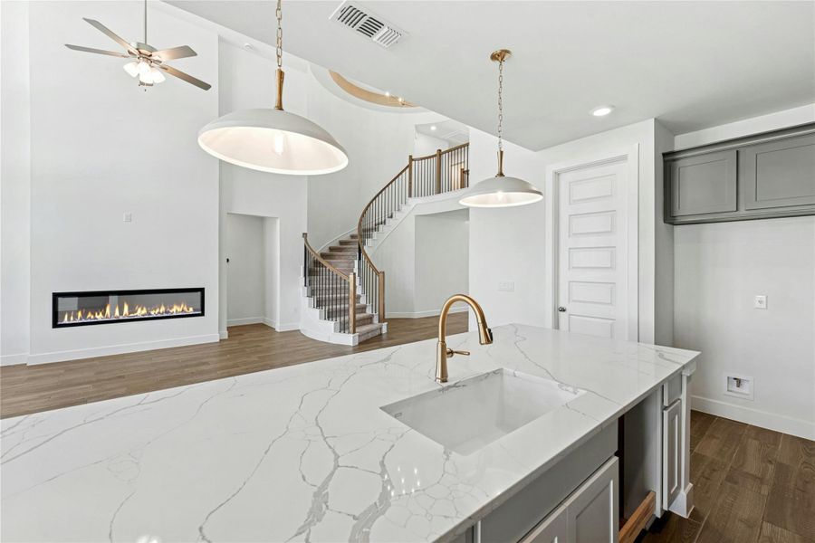 Kitchen featuring light stone countertops, dark wood-style floors, hanging light fixtures, a glass covered fireplace, and gray cabinetry