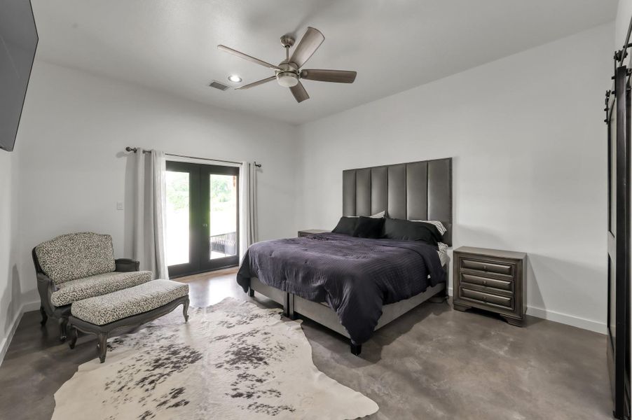 Spacious primary bedroom features a modern design.  Plenty of space for a cozy seating area, a ceiling fan, and natural light from glass doors leading to an outdoor space.