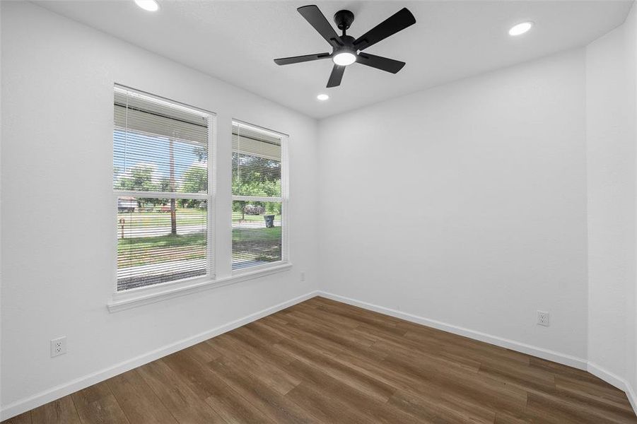 Room featuring wood-finish flooring, white walls, and dual windows with blinds Room featuring wood-finish flooring, white walls, and dual windows with blinds