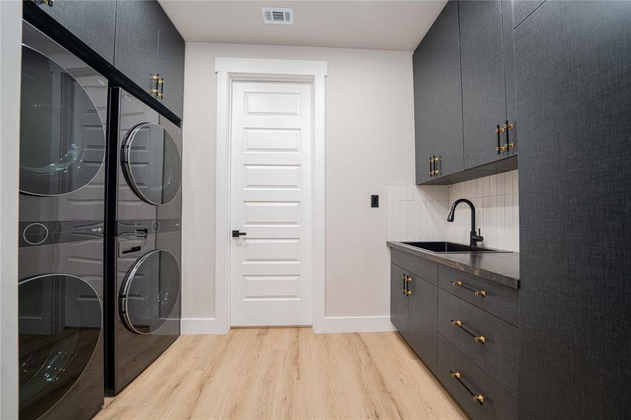 Laundry room featuring dark wood-finish cabinetry, light wood-finish flooring, a utility sink with a matte black faucet, and white subway tile backsplash