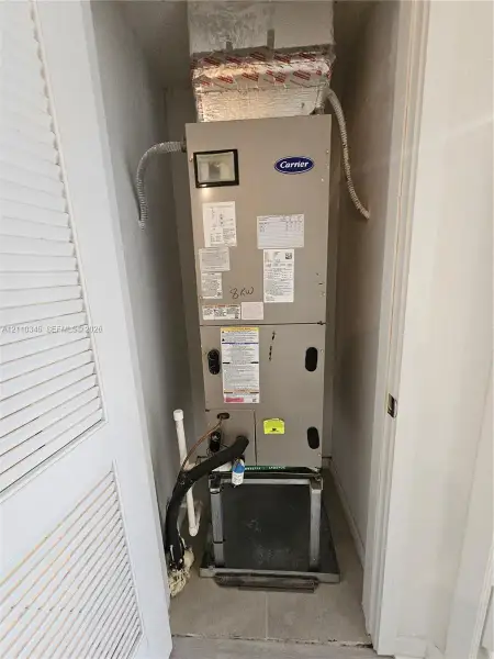 Carrier HVAC air handler unit featuring a metallic finish, mounted on a structural base, enclosed within a closet with louvered doors