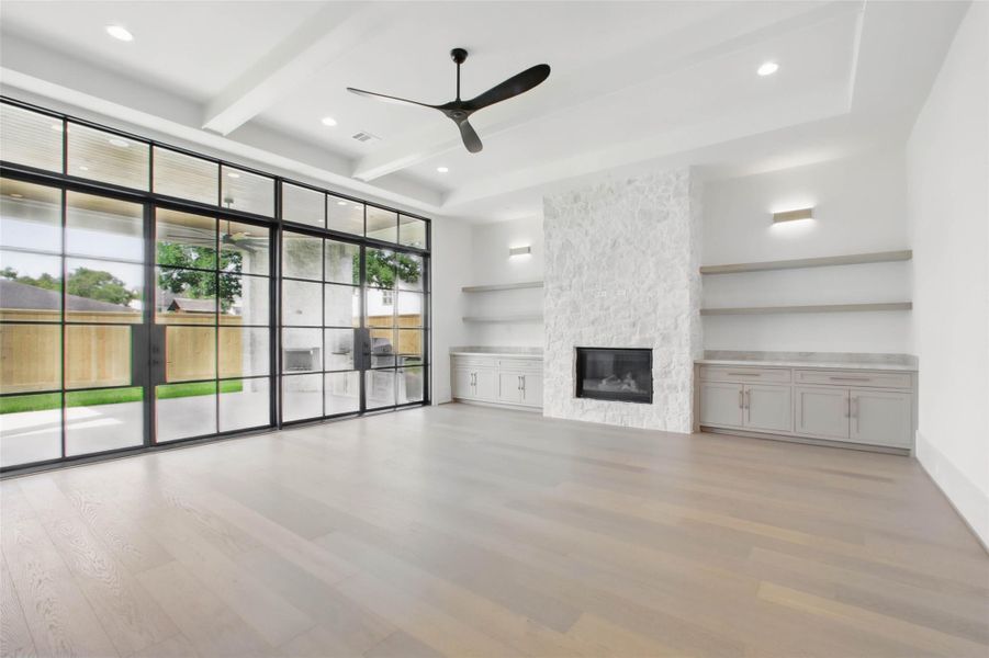 Sample of builder's previous construction. This home will have a similar family room layout as pictured here.  Wall of windows/doors leading to covered outdoor veranda/outdoor kitchen. Gas log fireplace with built-ins open shelving flanking either side. Buyer still has time to select finishes.
