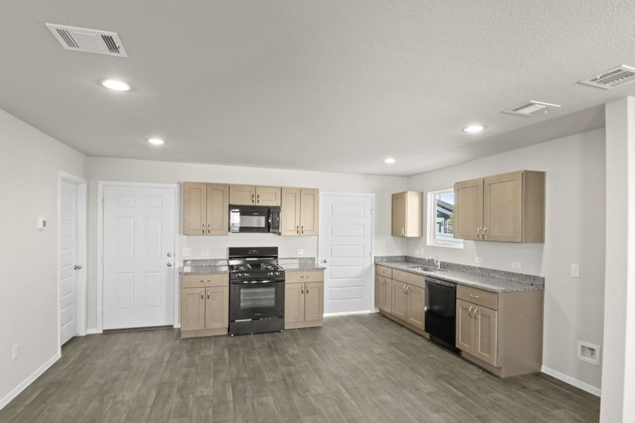 Image if a kitchen with light brown cabinets, granite countertops, and black appliances