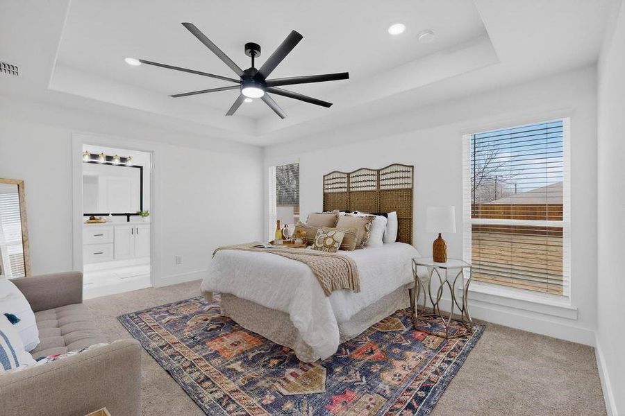 Primary bedroom featuring light colored carpet, a ceiling fan, and a tray ceiling Primary bedroom featuring light colored carpet, a ceiling fan, and a tray ceiling