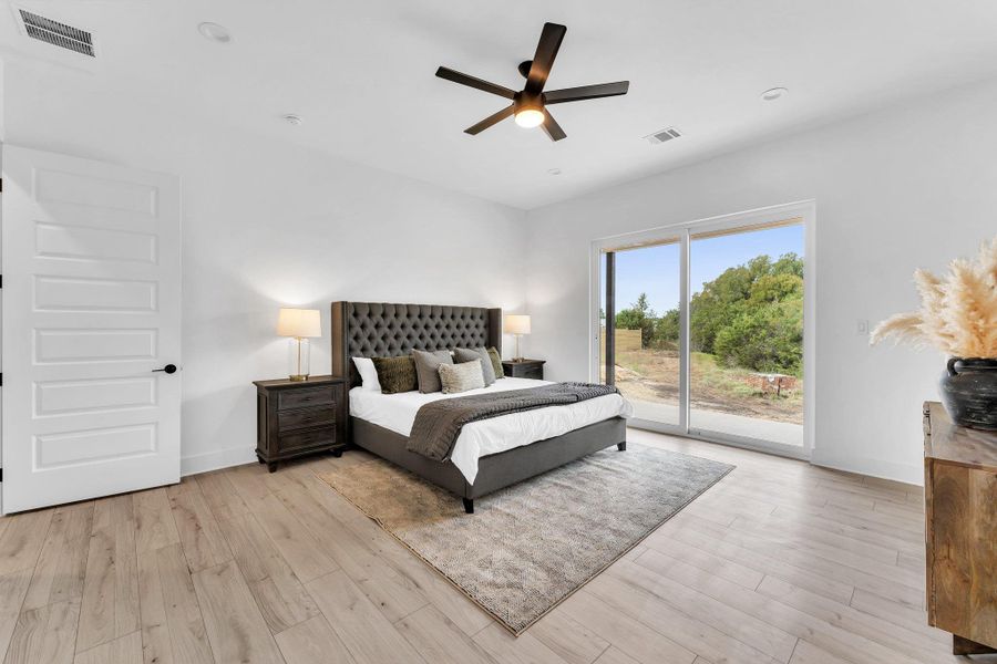 Sliding glass doors offer direct outdoor access from this well-lit bedroom featuring light wood flooring. Sliding glass doors offer direct outdoor access from this well-lit bedroom featuring light wood flooring.