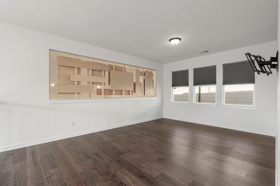 A well-lit, vacant room features rich hardwood flooring and contemporary window treatments.
