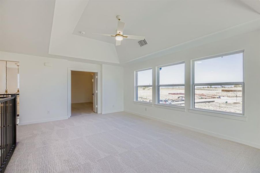 Unfurnished bedroom with light carpet, a ceiling fan, a tray ceiling, and a walk in closet