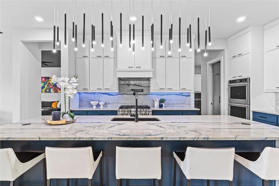 Kitchen with a kitchen bar, backsplash, white cabinets, light stone counters, and recessed lighting
