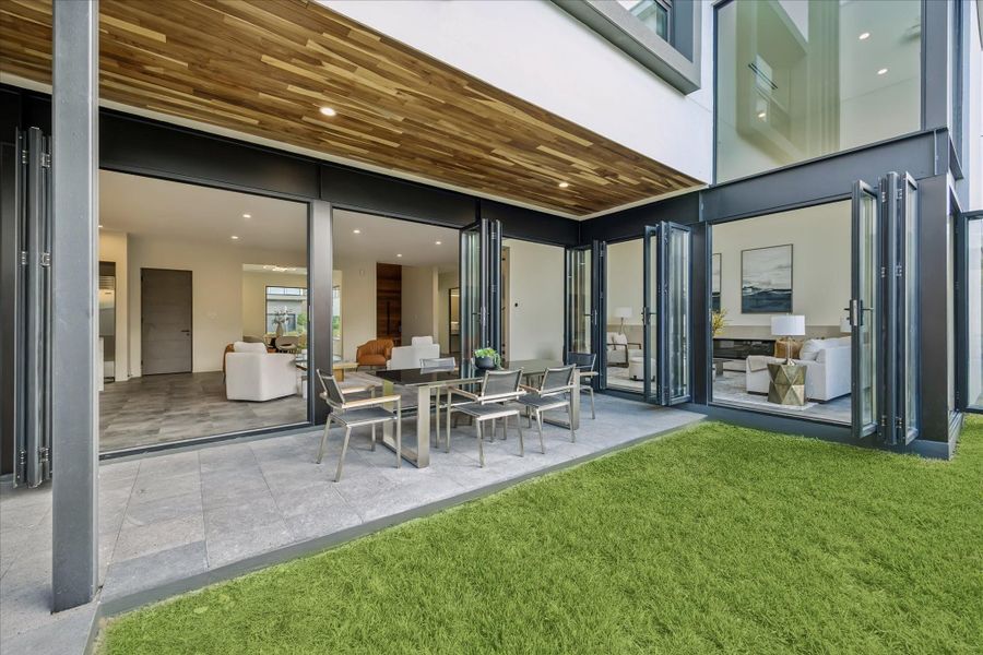 This modern home features expansive floor-to-ceiling glass doors that open to a spacious patio.