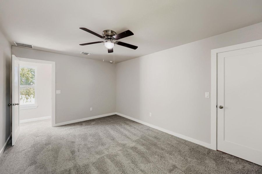 A well-lit bedroom with plush carpeting and a modern ceiling fan. A well-lit bedroom with plush carpeting and a modern ceiling fan.
