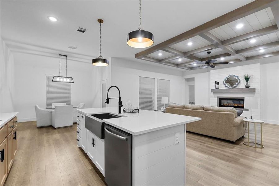 Kitchen featuring light hardwood / wood-style floors, white cabinets, a kitchen island with sink, stainless steel dishwasher, and decorative light fixtures