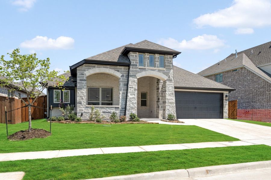 Two-story home with stone and brick exterior, arched entry, two-car garage, and green front lawn.