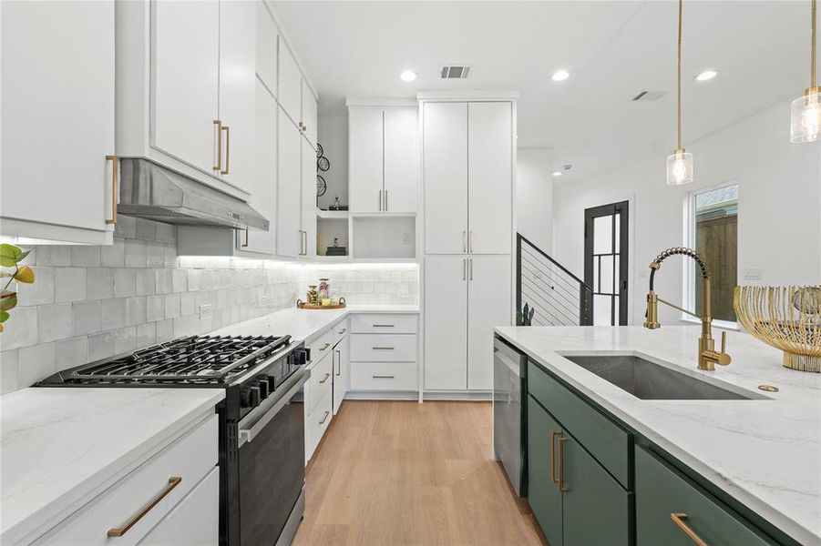 Kitchen with a sink, green cabinetry, gas range oven, dishwasher, and under cabinet range hood