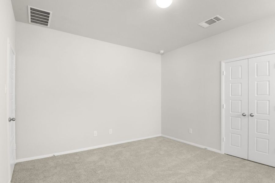 Image if a primary bedroom with tan carpeting, light grey walls, and double doors that lead to a primary bathroom