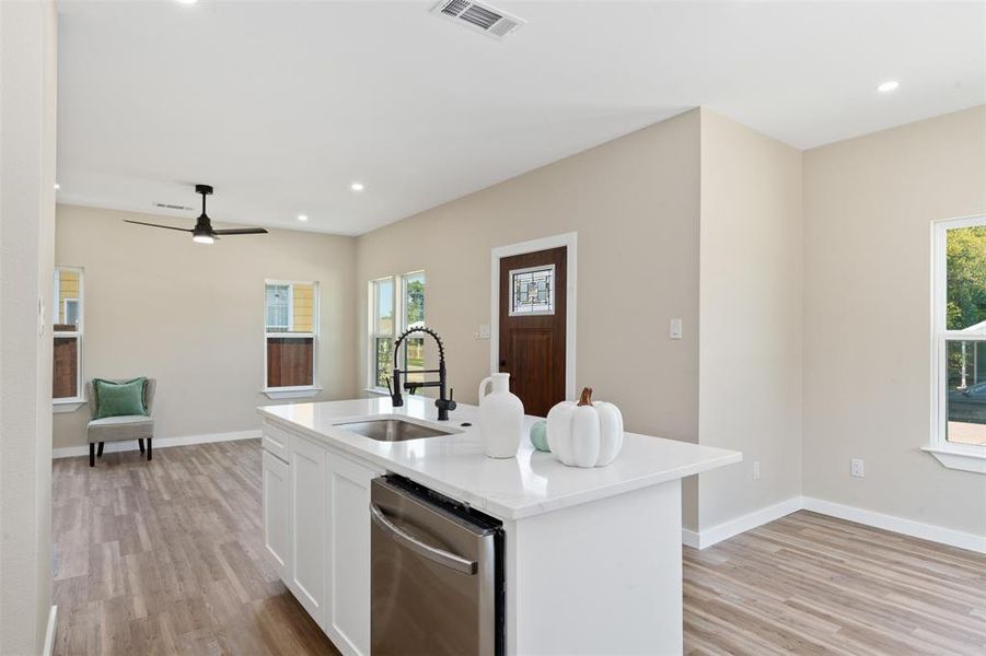 Kitchen featuring recessed lighting, a center island with sink, light stone counters, dishwasher, and light wood-style floors
