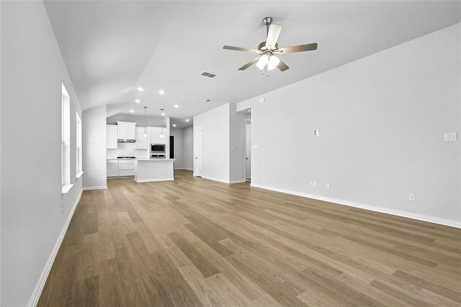 Unfurnished living room featuring ceiling fan, vaulted ceiling, light wood-type flooring, and recessed lighting Unfurnished living room featuring ceiling fan, vaulted ceiling, light wood-type flooring, and recessed lighting