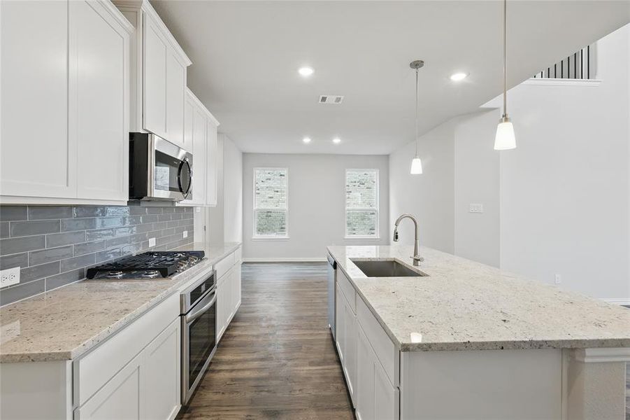 Kitchen with a center island with sink, dark wood-type flooring, white cabinetry, light stone counters, and recessed lighting