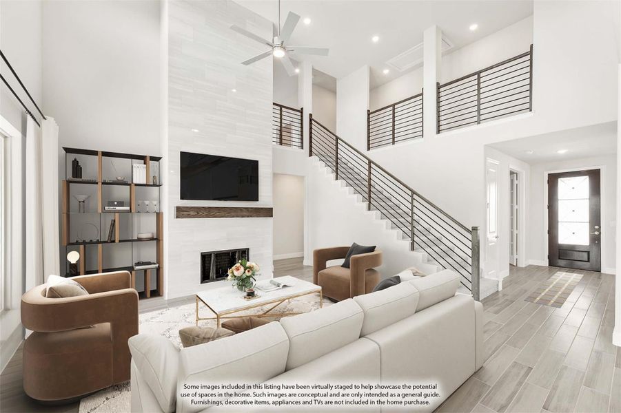 Open living room with two-story ceiling, fireplace, staircase, and ceiling fan over white sectional sofa Open living room with two-story ceiling, fireplace, staircase, and ceiling fan over white sectional sofa