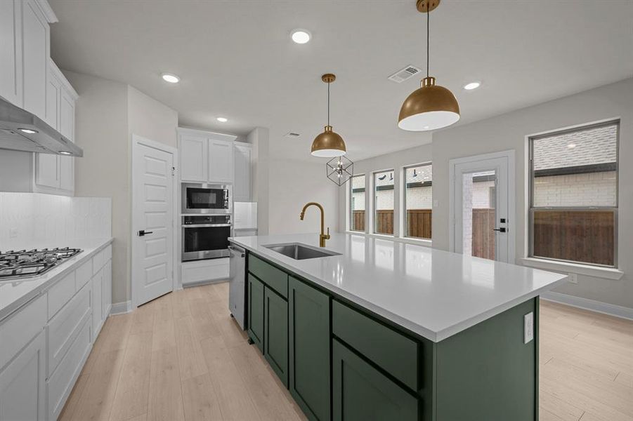 Dual tone kitchen featuring two tone cabinets, a kitchen island with sink, hanging light fixtures, light wood-style flooring, and stainless steel appliances