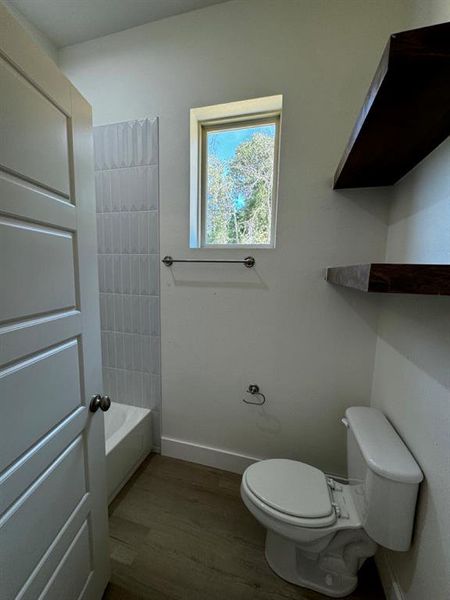 Bathroom with wood-type flooring,  shower combination, and toilet