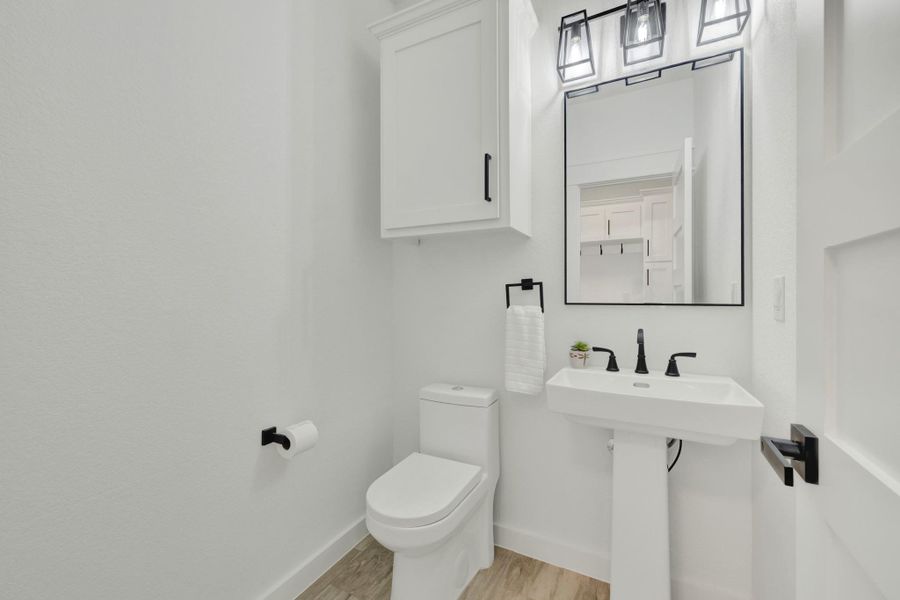 Half bath with pedestal sink with matte black faucet, framed mirror, and three-light vanity fixture