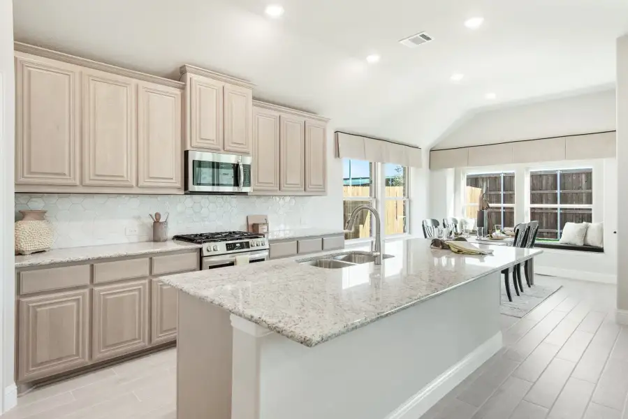 Kitchen with large granite island, beige cabinets, stainless steel appliances, and tile backsplash open to dining area