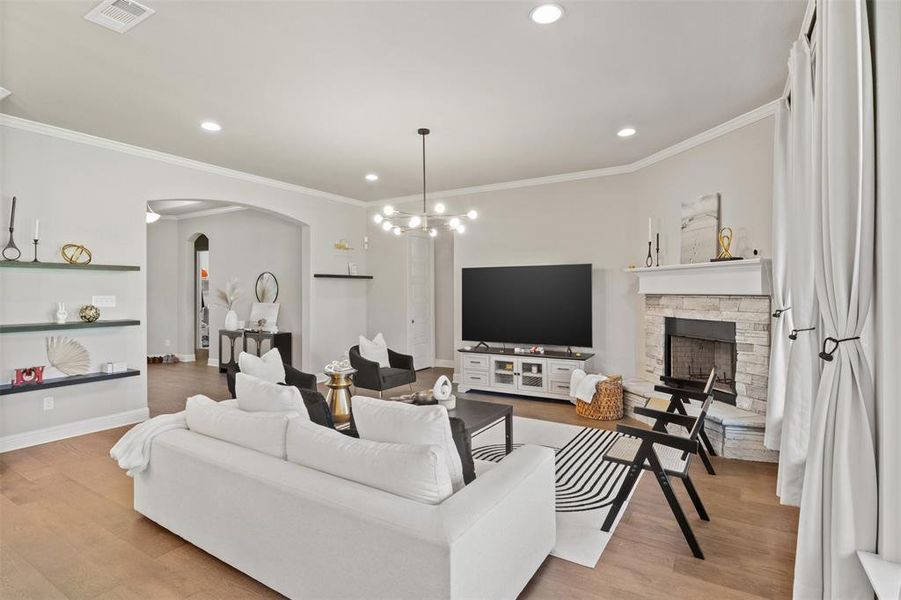 Living room with a notable chandelier, light hardwood / wood-style floors, crown molding, and a stone fireplace