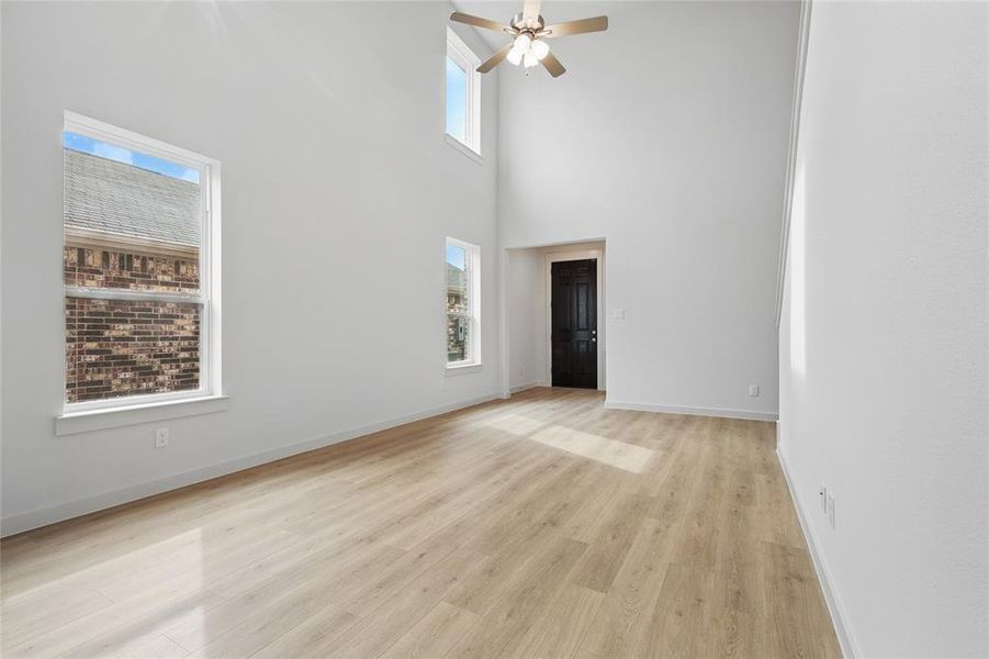 Unfurnished living room featuring ceiling fan, a high ceiling, and light wood-style flooring