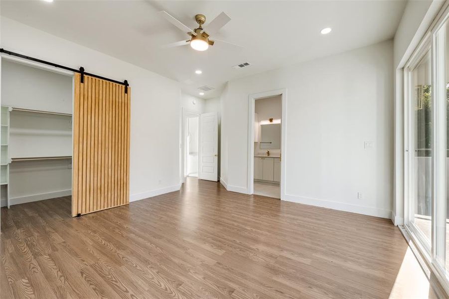 Unfurnished bedroom featuring recessed lighting, a barn door, light wood-style floors, a walk in closet, and ceiling fan Unfurnished bedroom featuring recessed lighting, a barn door, light wood-style floors, a walk in closet, and ceiling fan