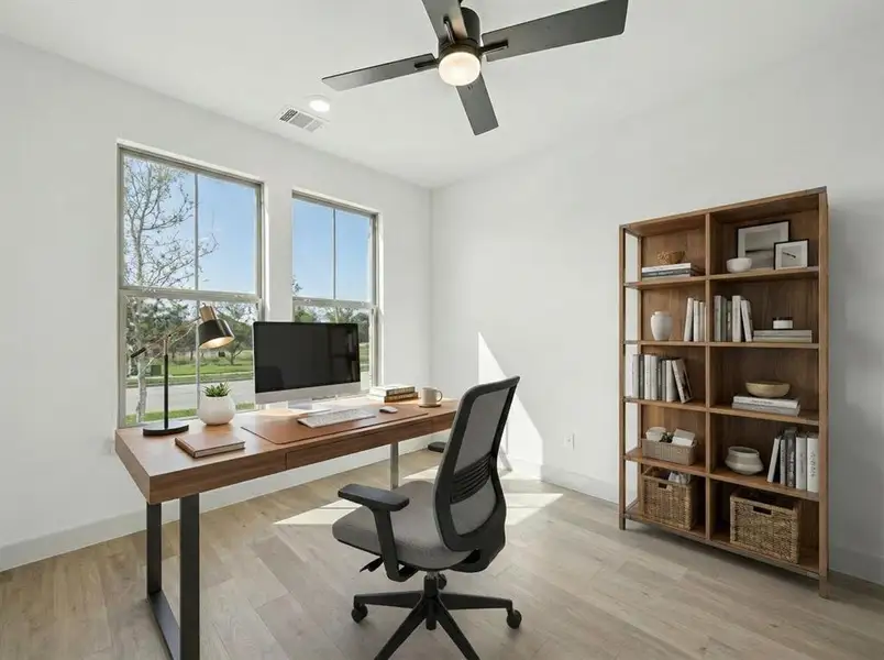 Bright room featuring two large windows, wood-finish flooring, a contemporary ceiling fan with integrated lighting, and a built-in shelving unit