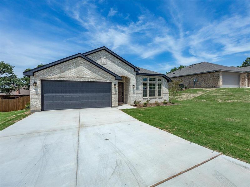 Brick exterior featuring a dark gray garage door, multiple windows, an established lawn, and a concrete driveway Brick exterior featuring a dark gray garage door, multiple windows, an established lawn, and a concrete driveway