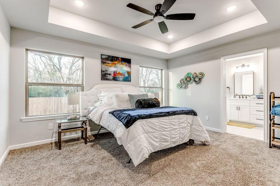 Carpeted bedroom with a raised ceiling, ensuite bathroom, and ceiling fan