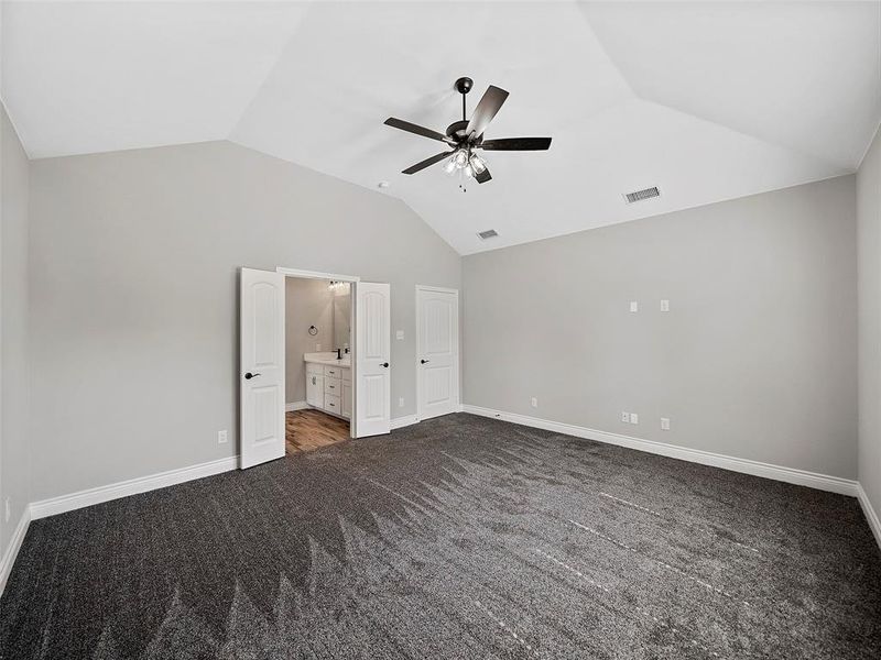 Unfurnished bedroom with lofted ceiling, ensuite bath, dark carpet, and a ceiling fan Unfurnished bedroom with lofted ceiling, ensuite bath, dark carpet, and a ceiling fan