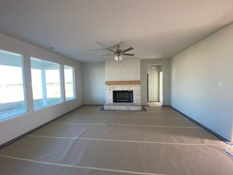 Spacious interior room featuring a stone-clad fireplace with a wood mantel, a ceiling fan, and a wall of multiple windows providing ample natural light