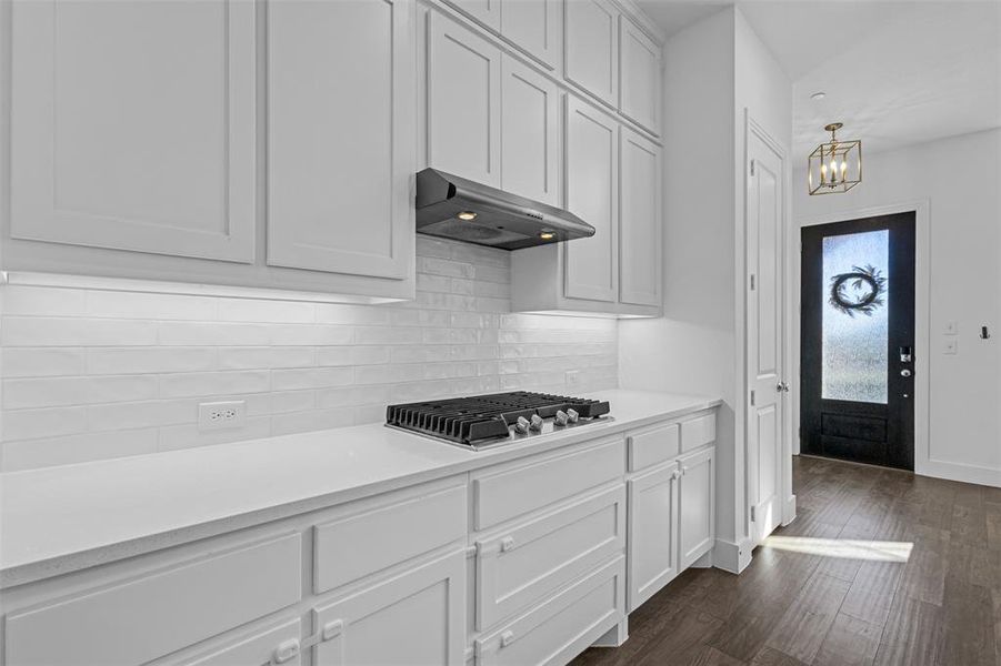 Kitchen with tasteful backsplash, white cabinets, dark wood-style floors, stainless steel gas stovetop, and under cabinet range hood