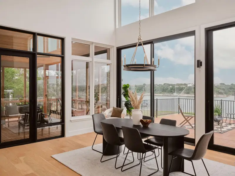 High ceilings featuring an ornate chandelier, expansive windows with black framing, wood-finish flooring, and a large outdoor deck with metal railing