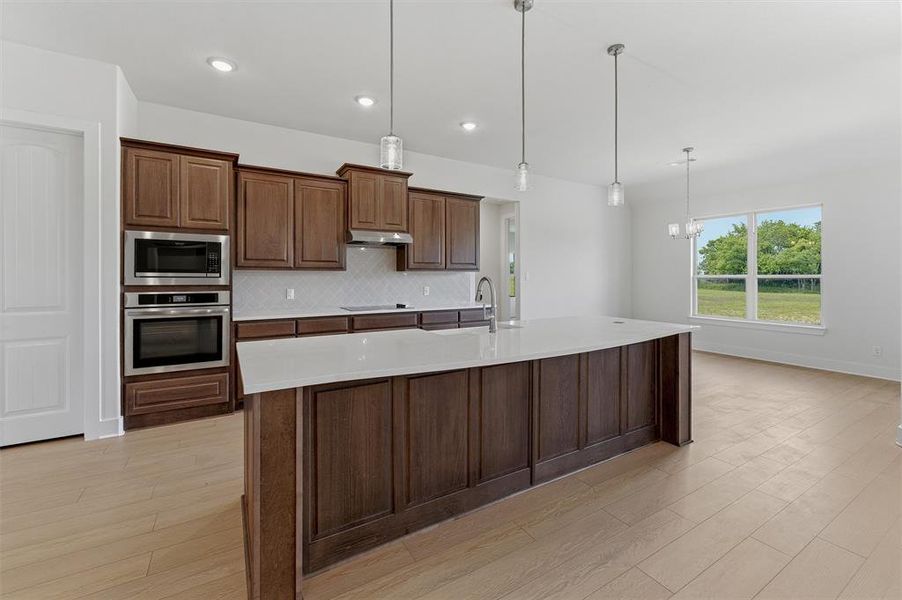 Spacious kitchen featuring an expansive island with a white countertop, rich wood cabinetry, stainless steel appliances, and wood-finish flooring Spacious kitchen featuring an expansive island with a white countertop, rich wood cabinetry, stainless steel appliances, and wood-finish flooring